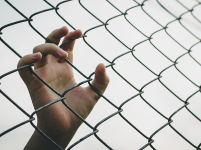 Youth's hand grasping fence