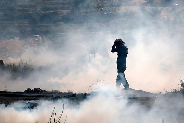A Palestinian man wears a gas mask as he walks in the smoke during a protest in the West Bank city of Ramallah on April 6, 2018. Clashes erupted on the Gaza-Israel border Friday, a week after Israeli forces killed 19 Palestinians at similar demonstrations.