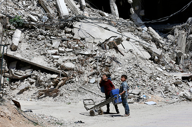 Syrian boys walk along a destroyed street in Douma on the outskirts of Damascus on April 16, 2018, during an organized media tour.