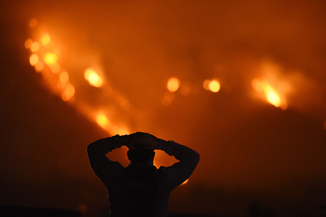 A man watches the Thomas Fire in the hills above Carpinteria, California, December 11, 2017. The Thomas Fire in California's Ventura and Santa Barbara counties has consumed more than 230,000 acres over the past week making it the fifth largest fire in the state's history.