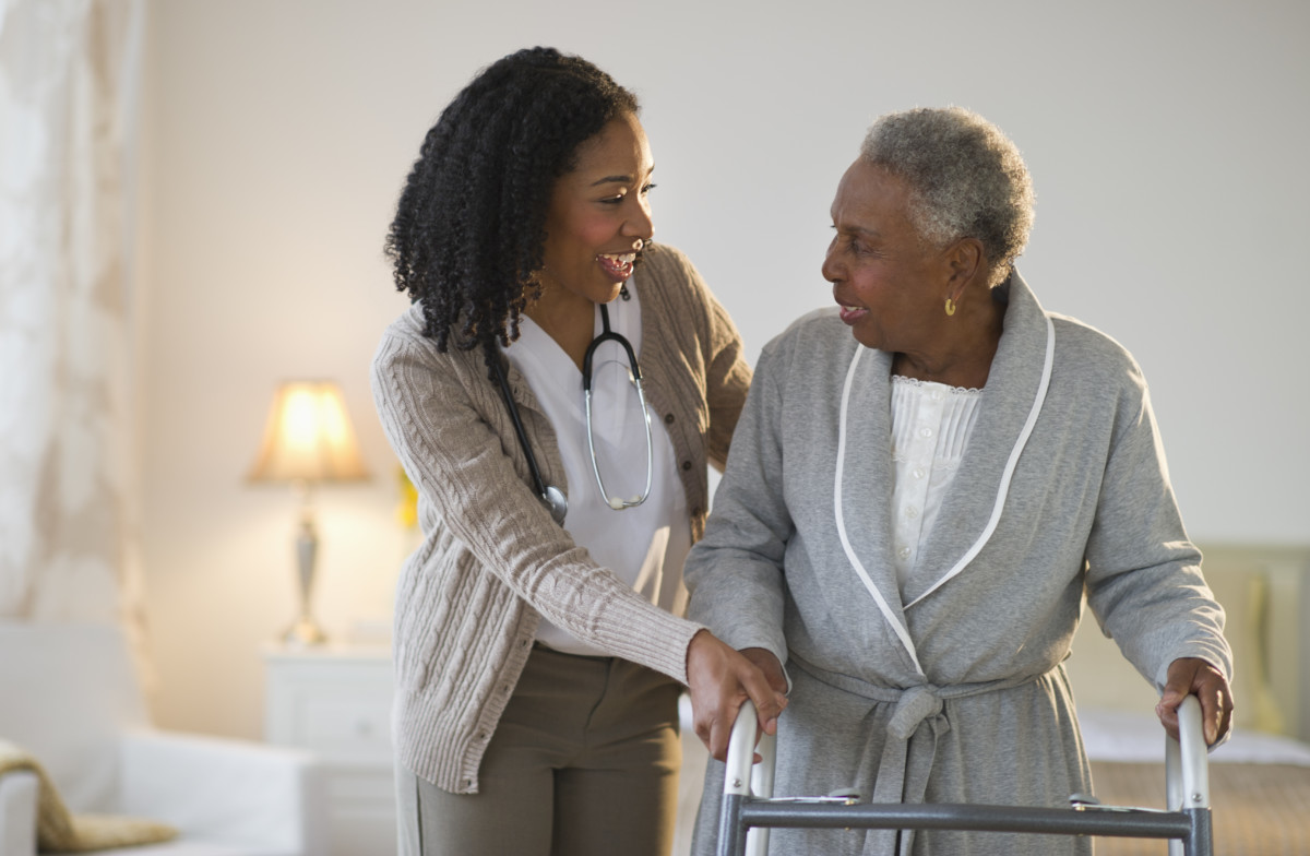 Nurse helping woman walk with walker.