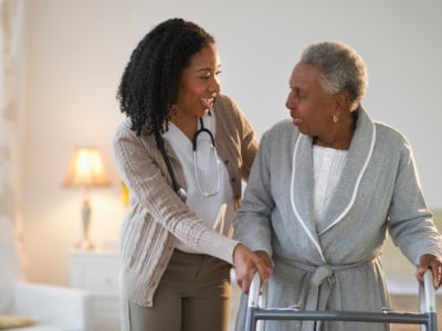 Nurse helping woman walk with walker.