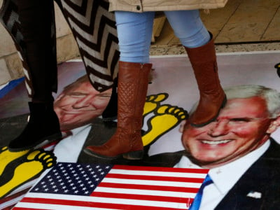 Palestinians walk on a poster bearing images of Donald Trump and his deputy Mike Pence during a demonstration at the al-Quds Open University in Dura village on the outskirts of the West Bank town of Hebron on December 13, 2017.