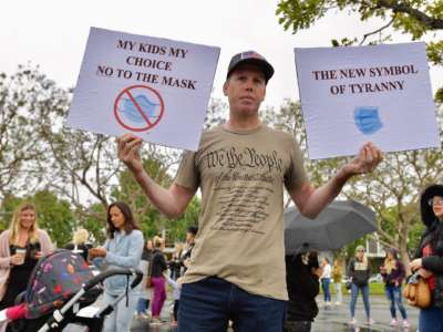 A man with no eyebrows displays signs comparing mask wearing to tyranny