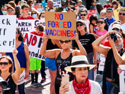A woman with a QAnon shirt and a "no forced vaccines" sign stands with protesters outside the Massachusetts State House in Boston on August 30, 2020.