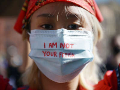 An Asian woman wears a mask with "I AM NOT YOUR FETISH" written across it