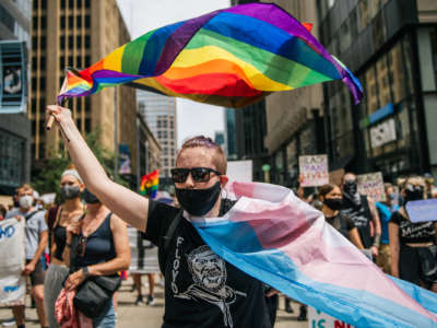 A marcher waves the trans and gay pride flags at a protest