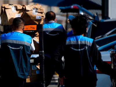 An Amazon delivery driver scans bags of groceries while loading a vehicle outside of a distribution facility on February 2, 2021, in Redondo Beach, California.