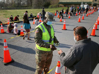 A member of the Maryland National Guard hands out Post-It notes with numbers to people arriving without appointments at the mass coronavirus vaccination site at Hagerstown Premium Outlets on April 7, 2021, in Hagerstown, Maryland.