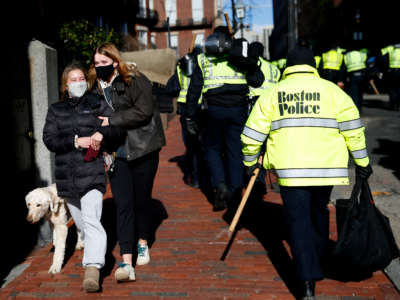 Girls walking a dog down Joy Street react as they pass by hundreds of Boston Police officers, who arrived in busses on Beacon Street and made their way towards the Massachusetts State House ahead of concerns over a protest by far right groups in Boston on January 17, 2021.
