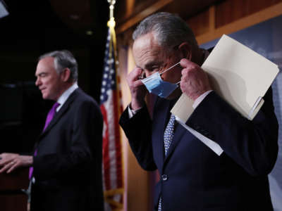 Senate Minority Leader Charles Schumer, right, replaces his surgical mask after yielding the lectern to Sen. Tim Kaine during a news conference at the U.S. Capitol on November 17, 2020, in Washington, D.C.