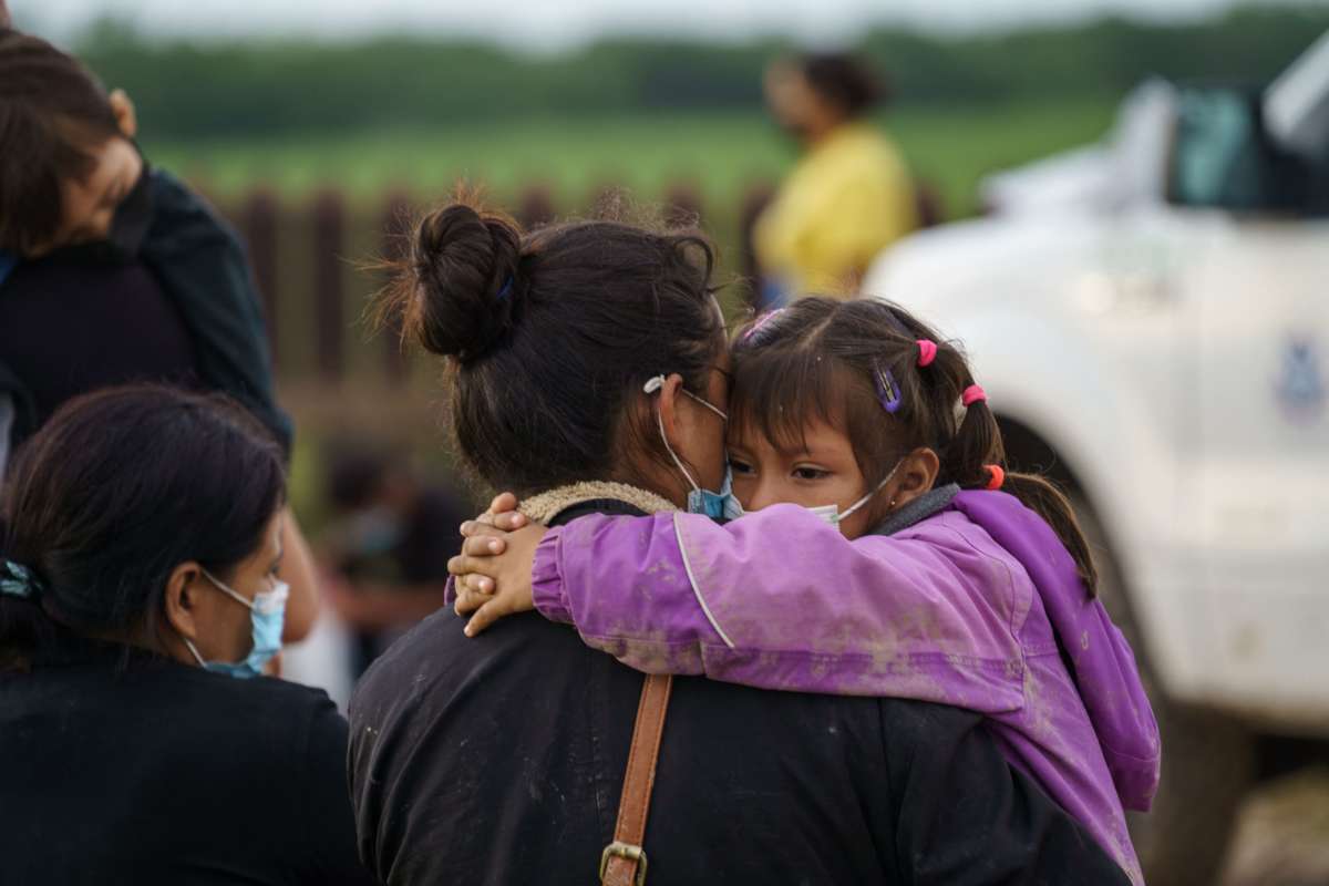 A little girl hugs her mom's neck as she's carried