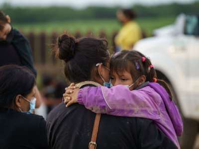 A little girl hugs her mom's neck as she's carried