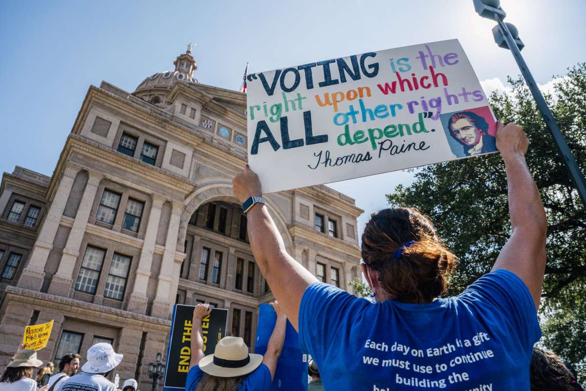 A protester holds a sign reading "VOTING IS THE RIGHT UPON WHICH ALL OTHER RIGHTS DEPEND" during a protest