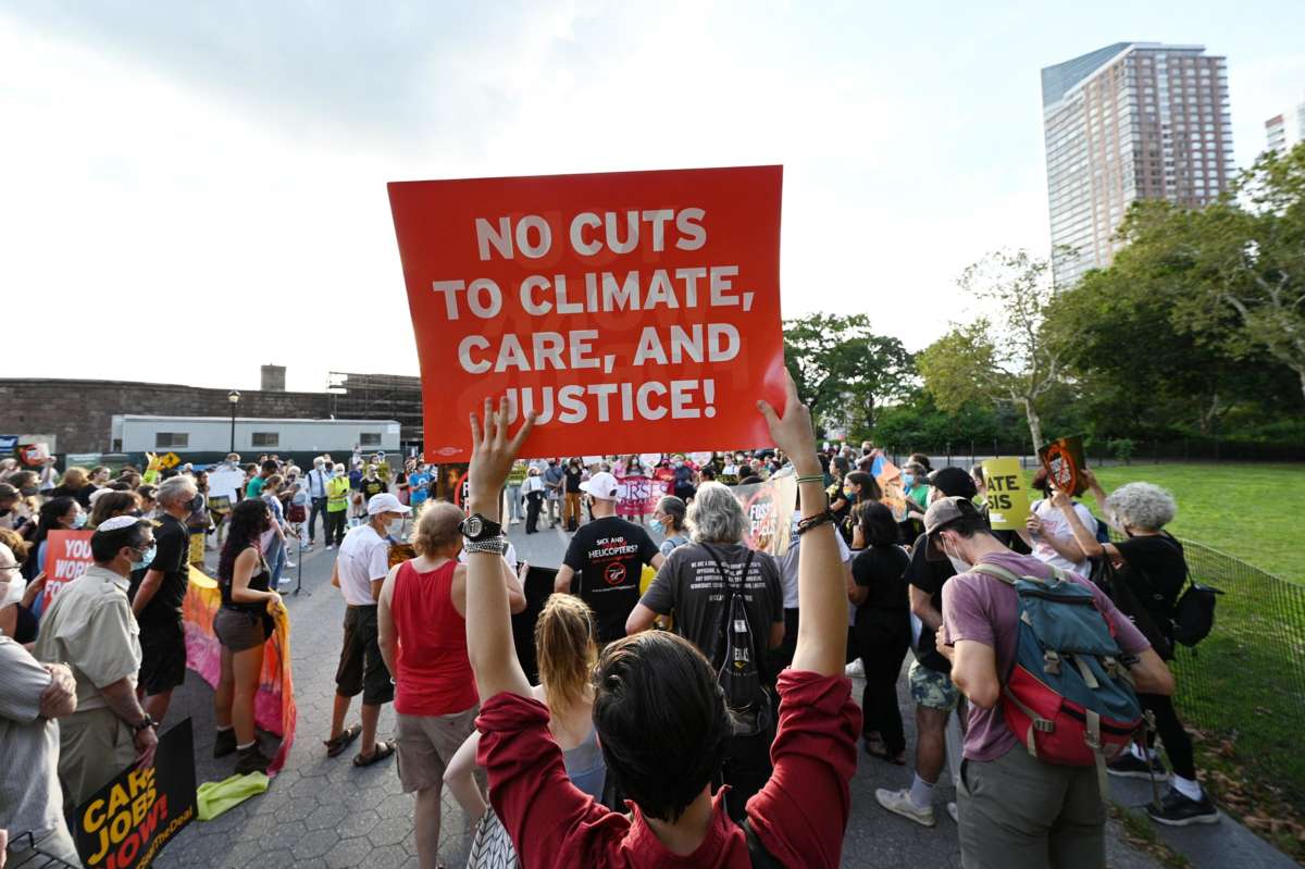 A protester holds a sign reading "NO CUTS TO CLIMATE, CARE AND JUSTICE!" during a demonstration