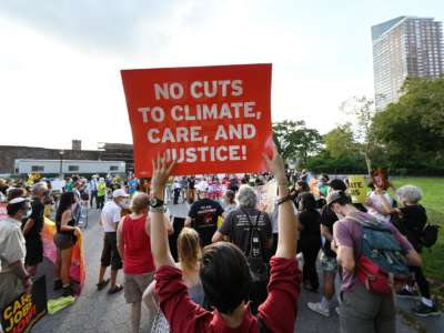 A protester holds a sign reading "NO CUTS TO CLIMATE, CARE AND JUSTICE!" during a demonstration