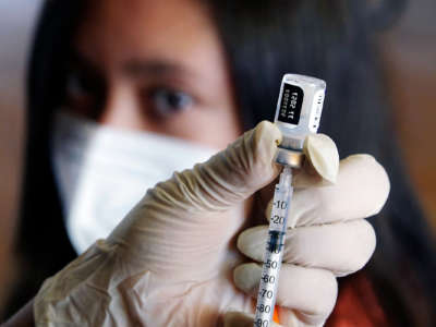 A medical worker fills a syringe with the pfizer/biontech vaccine as their patient looks onward in the background