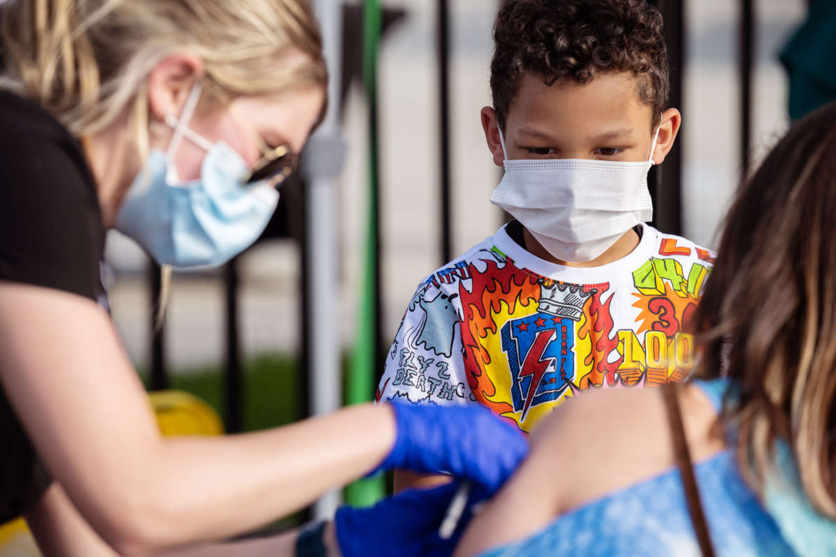 A child watches a healthcare worker administer the covid-19 vaccine to a patient