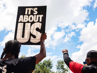 People display signs, one of which reads "IT'S ABOUT US," during a protest