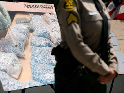 An officer stands in front of a displayed photograph showing counterfeit fentanyl pills during a press conference on May 13, 2021, in Los Angeles, California.