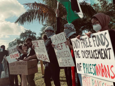 Protesters hold signs in front of the Duty Free Americas headquarters in South Florida.