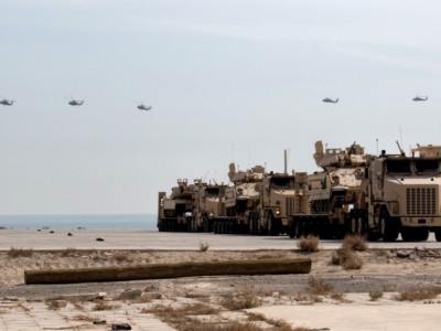 UH-60 Black Hawk helicopters fly over armored vehicles that have been loaded onto trucks for transport on February 9, 2018, at the Kuwait Naval Base.