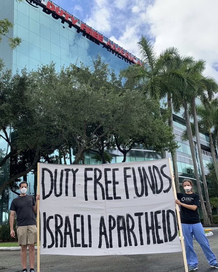 Protesters hold a sign reading "Duty Free Funds Israeli Apartheid" in front of the Duty Free Americas headquarters.