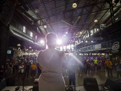 A woman is silhouetted by a spotlight as she speaks to a crowd of supporters from a stage