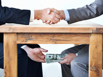 Cropped shot of two businessmen shaking hands while money passes hands under a table