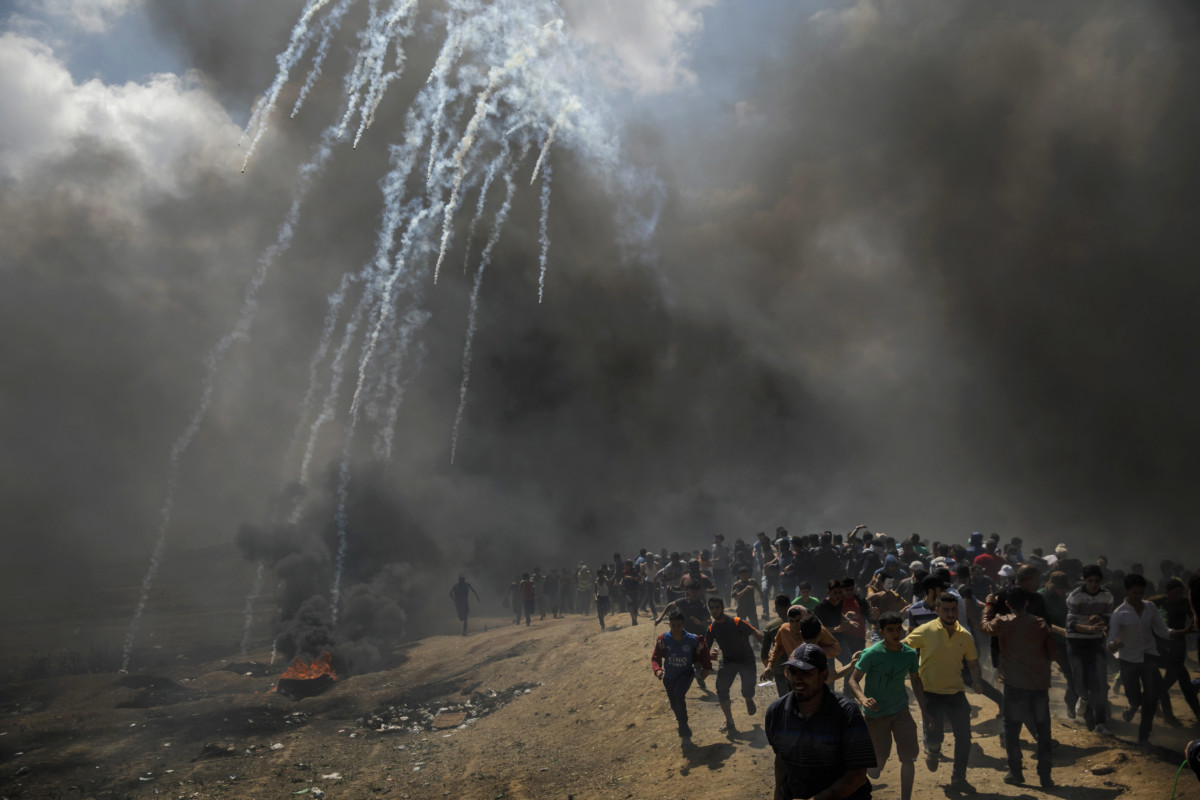 Protesters run away from tear gas dispersed by Israeli forces as they inch closer to the border fence separating Israel and Gaza on May 14, 2018, in a camp east of Gaza City, Gaza.