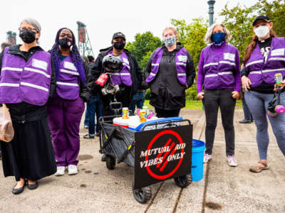 People smile for a photo behind a cart bearing a sign reading "MUTUAL AID VIBES ONLY"