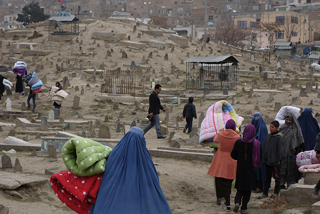 Bearing quilted bed covers, Afghans walk through the cemetery to their mountainside homes. (Photo: Courtesy of Carolyn Coe)