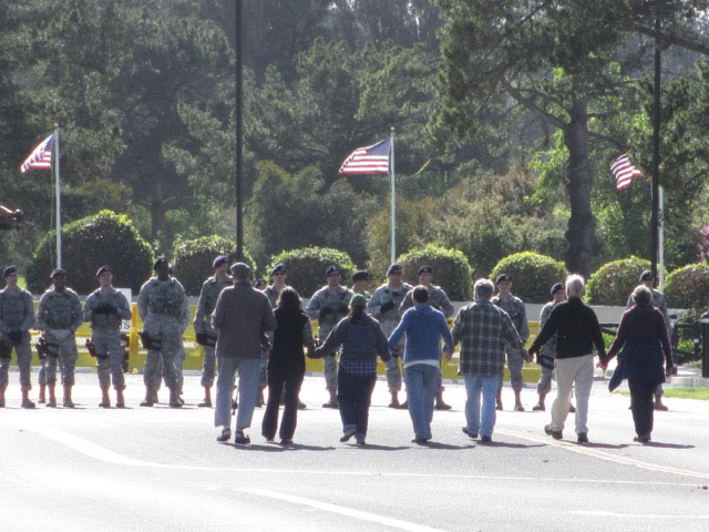 Seven Pacific Life Community members confront a line of security personnel at the entrance gate of Vandenberg Air Force Base in California on March 6, 2016, just prior to their arrest. From left: Charley Smith, Elizabeth Murray, Karan Benton, Jorge Manly-Gil, Ed Ehmke and Mary Jane Parrine. (Photo: Felice Cohen-Joppa of The Nuclear Resister)