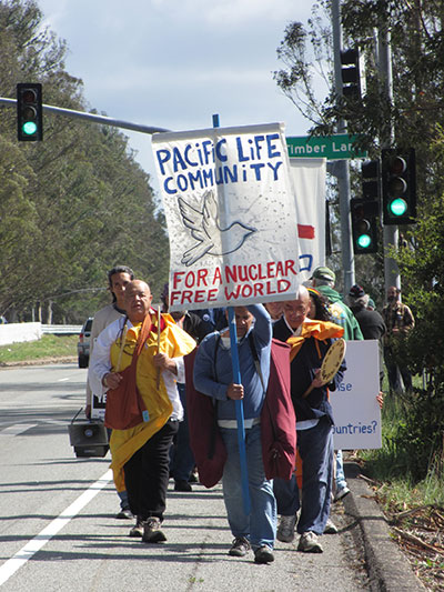 Buddhist monks Gilberto Zamora Perez, left, and Senji Kanaeda, right, flank a Pacific Life Community nuclear resistance sign as they approach Vandenberg Air Force Base for a protest action held in front of the base on Sunday, March 6, 2016. (Photo: Felice Cohen-Joppa of The Nuclear Resister)