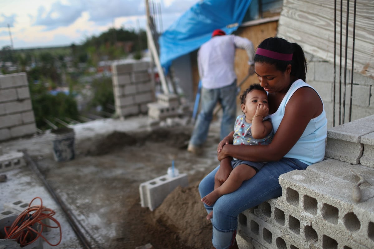 Mother Isamar holds her baby Saniel, 9 months, as husband Samuel mixes cement at their makeshift home, under reconstruction, after being mostly destroyed by Hurricane Maria, on December 23, 2017, in San Isidro, Puerto Rico.