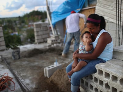 Mother Isamar holds her baby Saniel, 9 months, as husband Samuel mixes cement at their makeshift home, under reconstruction, after being mostly destroyed by Hurricane Maria, on December 23, 2017, in San Isidro, Puerto Rico.