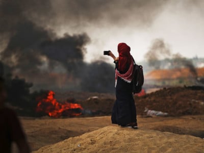 A Palestinian woman documents the situation at the border fence with Israel as mass demonstrations continue on May 14, 2018, in Gaza City, Gaza.