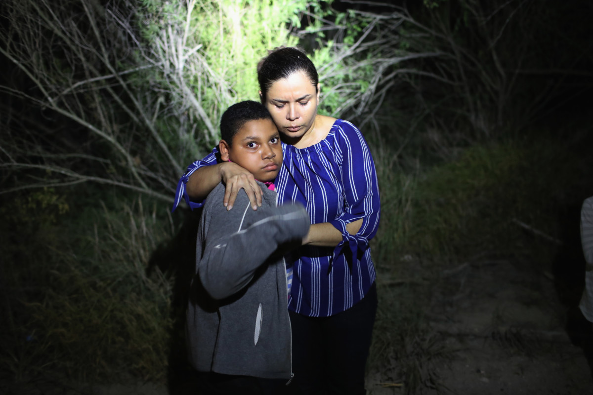 A US Border Patrol spotlight shines on a terrified mother and son from Honduras as they are found in the dark near the US-Mexico border on June 12, 2018, in McAllen, Texas. The asylum seekers had rafted across the Rio Grande from Mexico and had become lost in the woods. They were then detained by Border Patrol agents and then sent to a processing center for possible separation.