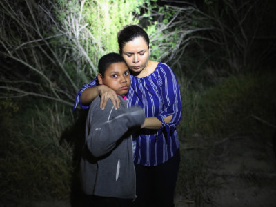 A US Border Patrol spotlight shines on a terrified mother and son from Honduras as they are found in the dark near the US-Mexico border on June 12, 2018, in McAllen, Texas. The asylum seekers had rafted across the Rio Grande from Mexico and had become lost in the woods. They were then detained by Border Patrol agents and then sent to a processing center for possible separation.