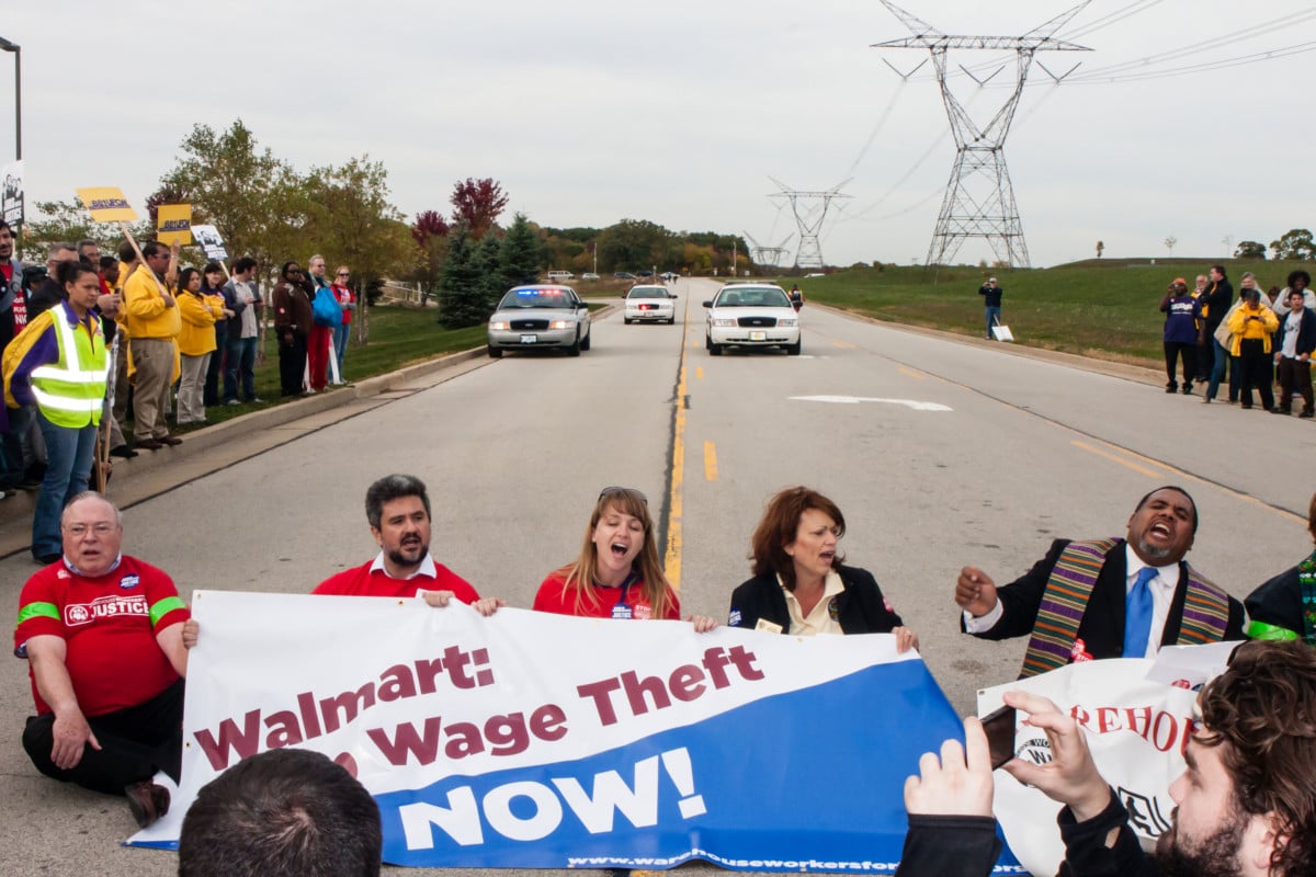 Protesters, including clergy members, stage a sit-down protest to block the entrance of the Walmart distribution center at a rally for Warehouse Workers Justice, October 1, 2012