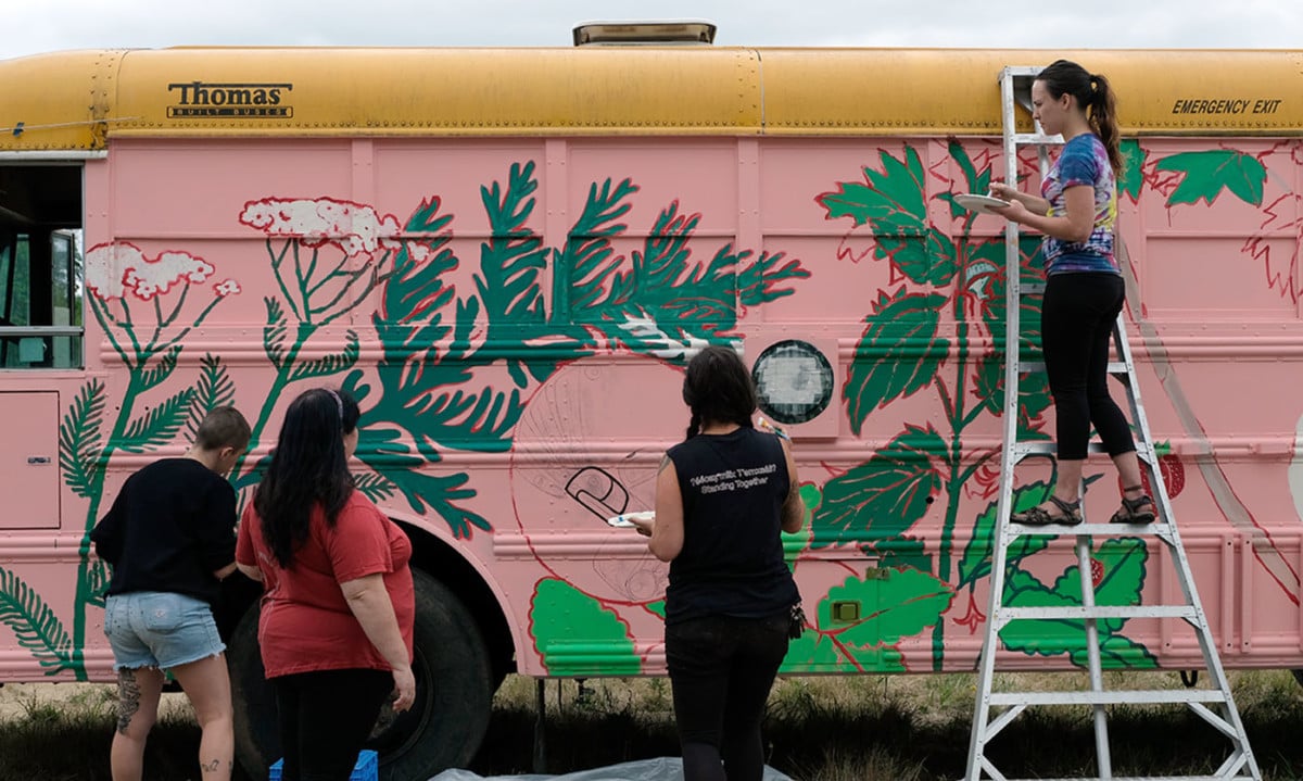 Volunteers paint the exterior of the Canoe Journey Herbalist bus during the Protecting Mother Earth conference at Frank's Landing, Washington.