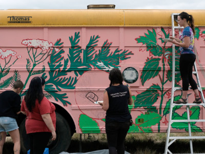 Volunteers paint the exterior of the Canoe Journey Herbalist bus during the Protecting Mother Earth conference at Frank's Landing, Washington.
