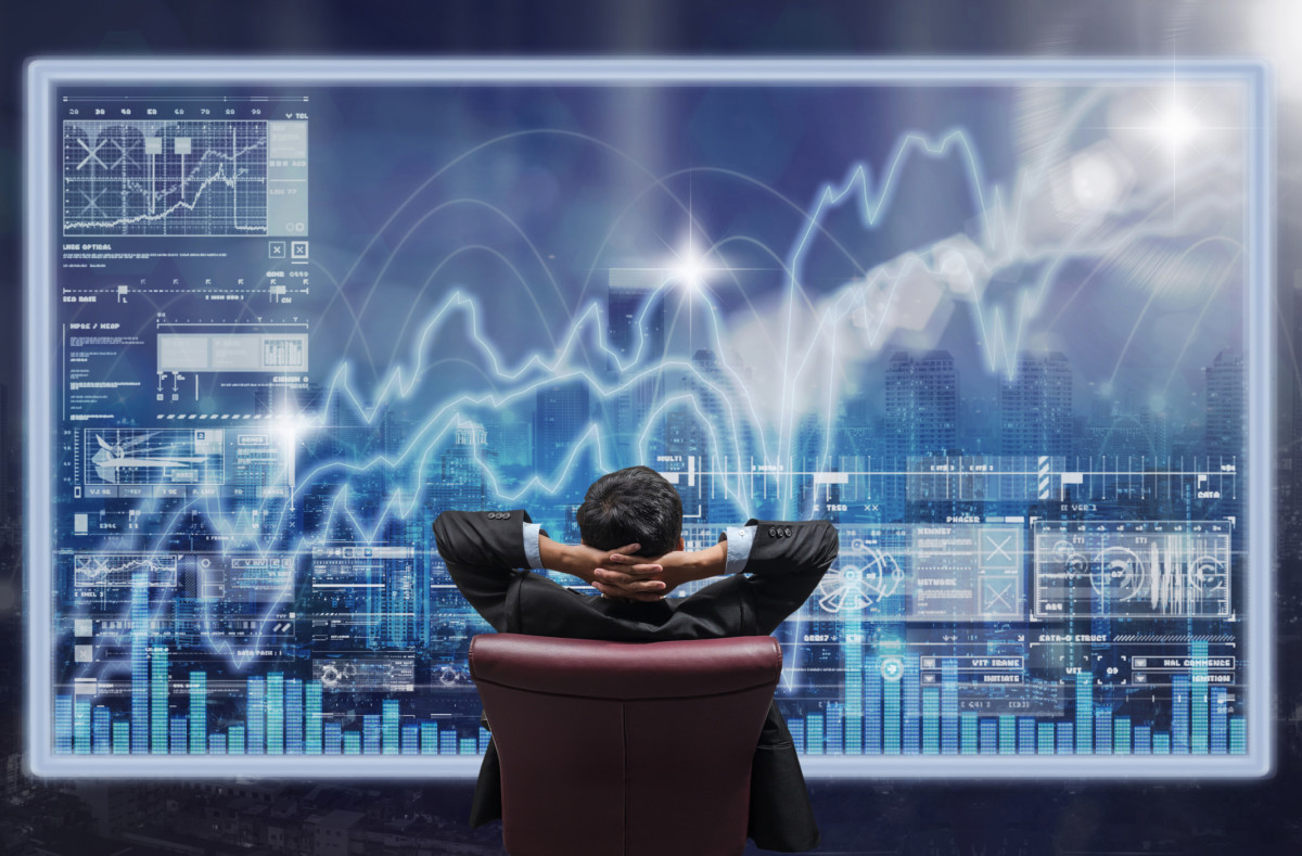 A business man looks at a virtual screen with data imposed over a cityscape.