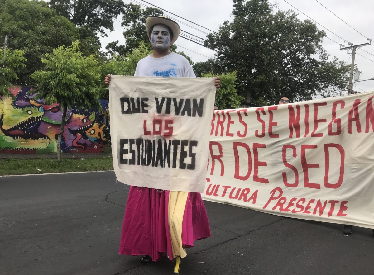 A demonstrator on stilts carries a sign reading “Long live students” during a march against water privatization in San Salvador, July 5, 2018.