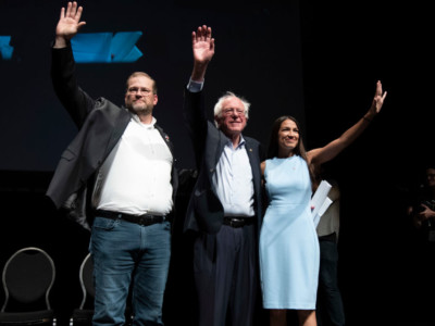 James Thompson, Sen. Bernie Sanders and Alexandria Ocasio-Cortez, wave to the crowd at the end of a campaign rally in Wichita, Kansas on July 20, 2018.