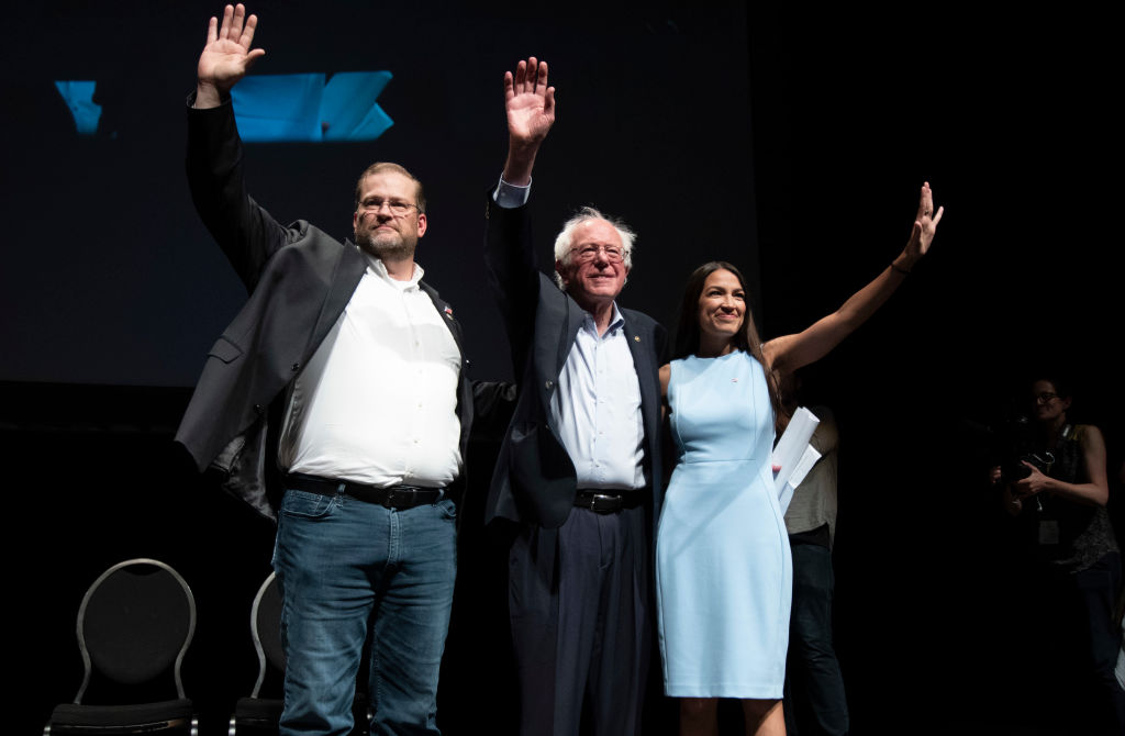 James Thompson, Sen. Bernie Sanders and Alexandria Ocasio-Cortez, wave to the crowd at the end of a campaign rally in Wichita, Kansas on July 20, 2018.