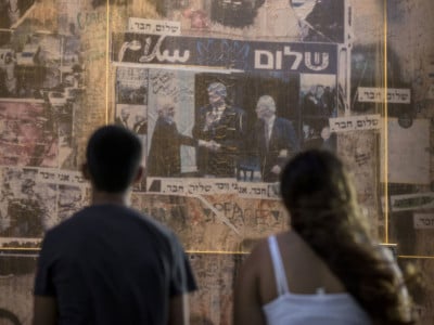 People look at a 20-year-old picture of late Israeli Prime Minister Yitzhak Rabin (right) shaking hands with late Jordanian King Hussein (left) while former President Bill Clinton applauds, framed by the words "peace" in Arabic and Hebrew. The photo is a memorial in the place where Rabin was assassinated in the Israeli Mediterranean city of Tel Aviv in 1995.