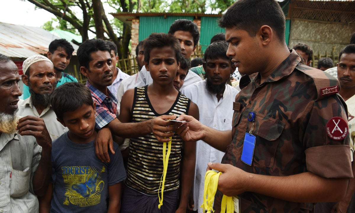 Rohingya refugees receive new ID cards from a soldier at the entrance to the Bangladeshi government registration office at the Kutupalong refugee camp near Ukhia on September 22, 2017.