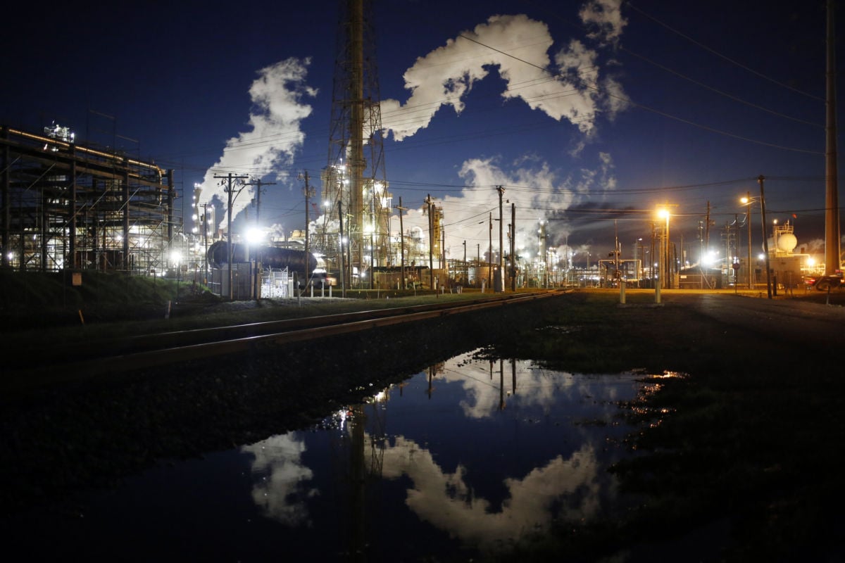 Emissions from an oil refinery are reflected in a street puddle at dusk in Texas.