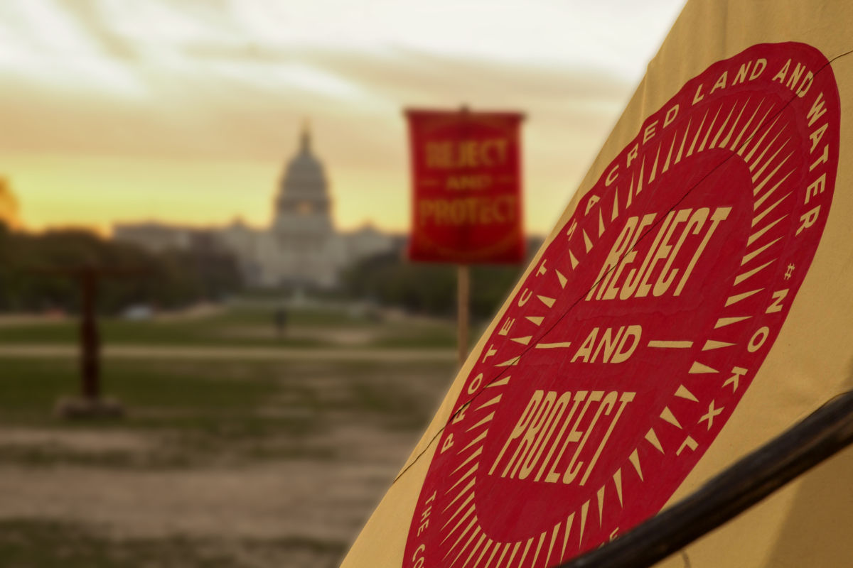 A red sign in front of the Capitol that says "Protect sacred lands and water #NoKXL" and "Reject and Protect"
